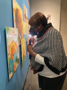 Valerie Frink of Jersey City, a VLANJ participant, closely inspects a bright, colorful work by artist Jerry Pinkney, using the flashlight on her mobile phone.