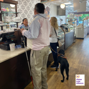 An individual holds a white cane while another has a guide dog at the checkout counter of a Morristown, NJ business.