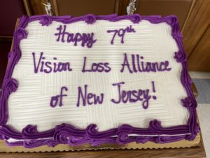 A white cake with purple frosting reads: "Happy 79th Vision Loss Alliance of New Jersey!"